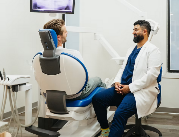 Dentist in white coat talking with a patient in a dental chair during consultation