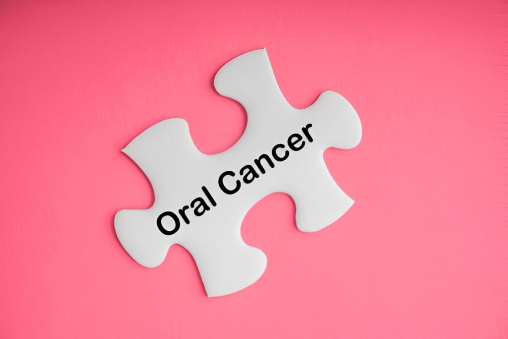White puzzle piece with the words “Oral Cancer” on a pink background