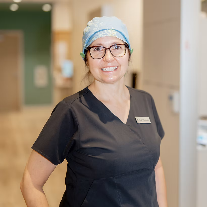 Smiling dental hygienist in black scrubs and blue surgical cap with glasses